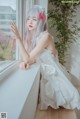 A woman in a white dress sitting by a window.