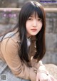 A young woman with long black hair sitting on a rock.