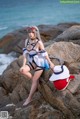 A woman in a sailor outfit sitting on a rock by the ocean.