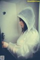 A woman in a white raincoat standing in a bathroom.