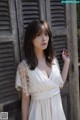 A woman in a white dress leaning against a wooden door.